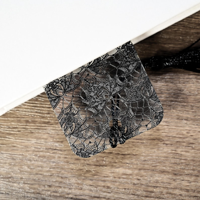 May include: Black lace bookmark with a tassel. The bookmark is made of clear plastic with a black lace design.