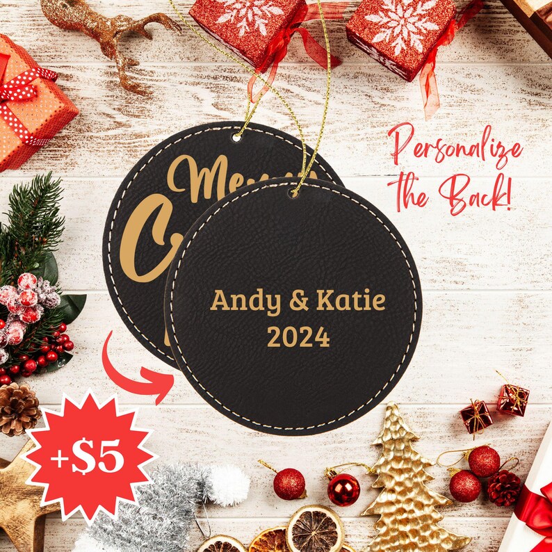 Może przedstawiać: Dwie czarne sk&oacute;rzane ozdoby choinkowe ze złotym przeszyciem. Ozdoba z przodu ma napis "Merry Christmas" złotymi literami. Ozdoba z tyłu ma napis "Andy & Katie 2024" złotymi literami.
