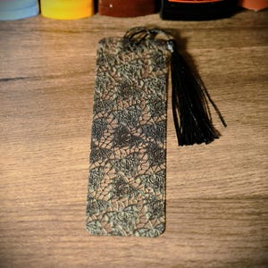 May include: A black and green bookmark with a lace pattern and a black tassel.