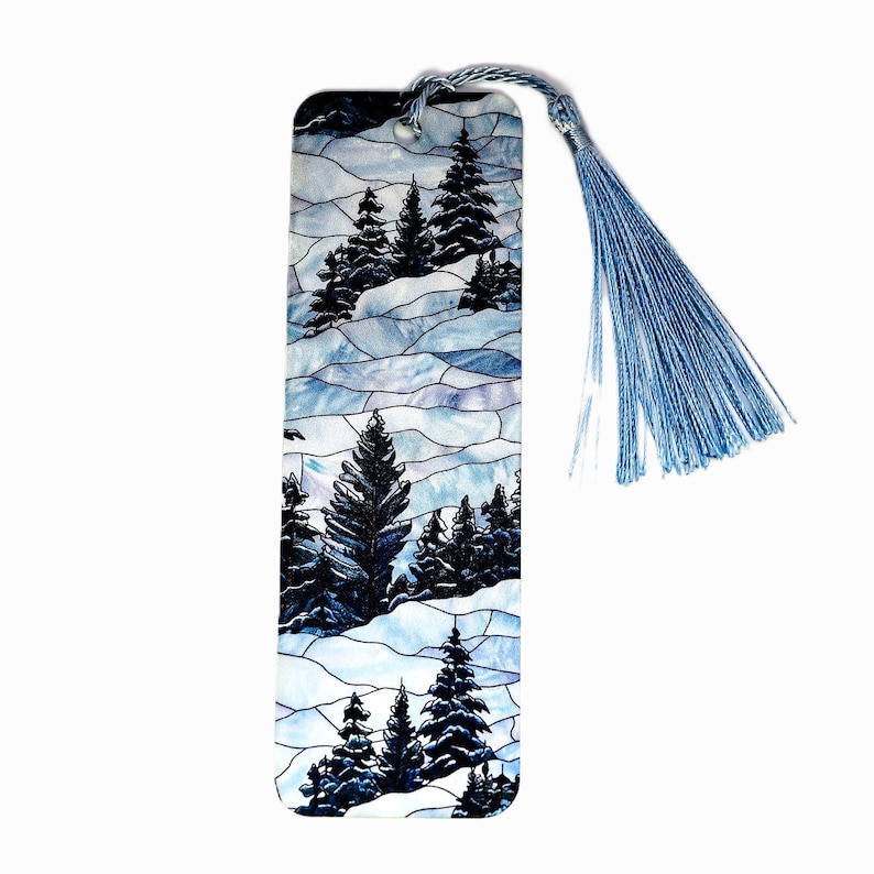 May include: A blue and white glass bookmark with a stained glass design of a winter forest scene. The bookmark has a blue tassel.