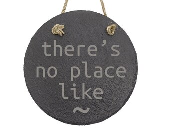 May include: Round, dark gray slate sign with the phrase "there's no place like" etched in light gray. The sign is suspended by a natural rope. A decorative item for the home.
