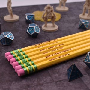 May include: A set of yellow pencils with pink erasers and green metal ferrules. Each pencil features black text including Eraser of Counterspelling, Cursed Wand of Rolling, Wand of Character Editing, Wand of Storytelling, Wand of Infinite Possibilities, and Wand of Intelligence.