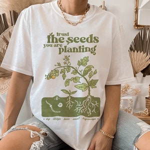 May include: White t-shirt with a green illustration of a plant with the text "trust the seeds you are planting. Big things have small beginnings."