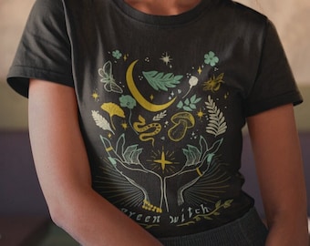 May include: A dark green t-shirt with a graphic design of a crescent moon, stars, leaves, and a snake. The text "Green Witch" is printed on the bottom of the design.