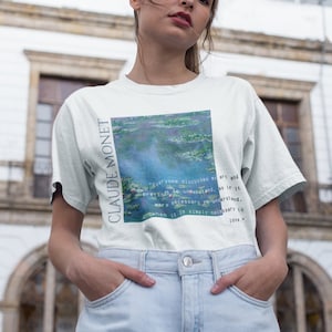 Pode incluir: Uma camiseta branca com uma imagem azul e verde de lírios d'água e o texto "Claude Monet" impresso na frente.