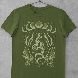 Pu&ograve; includere: Una maglietta verde con un designo verde chiaro di una mano che tiene un serpente, cristalli e una luna crescente con stelle.
