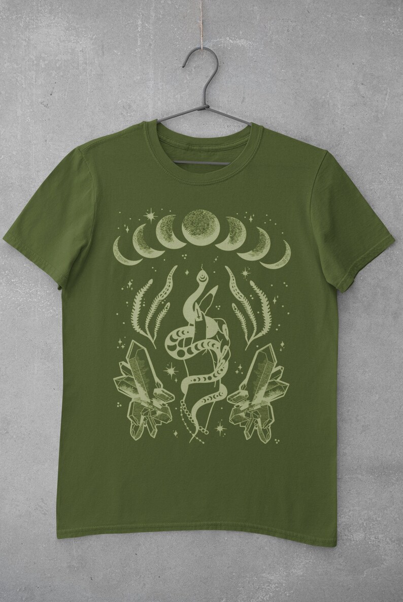 Pu&ograve; includere: Una maglietta verde con un designo verde chiaro di una mano che tiene un serpente, cristalli e una luna crescente con stelle.