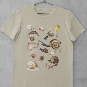 May include: A beige t-shirt with a graphic print of various snails in different sizes and colors. The snails are arranged in a random pattern on the shirt.