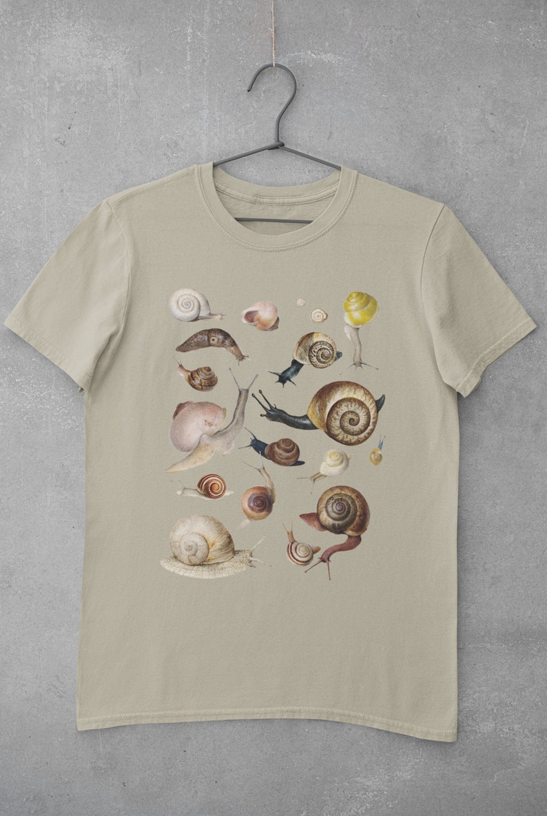 May include: A beige t-shirt with a graphic print of various snails in different sizes and colors. The snails are arranged in a random pattern on the shirt.