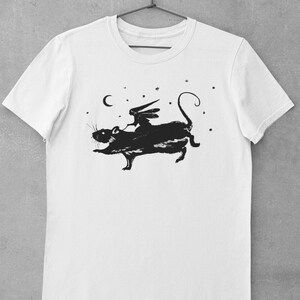 Puede incluir: Camiseta blanca con una silueta negra de un hada montando una rata bajo una luna creciente y estrellas.