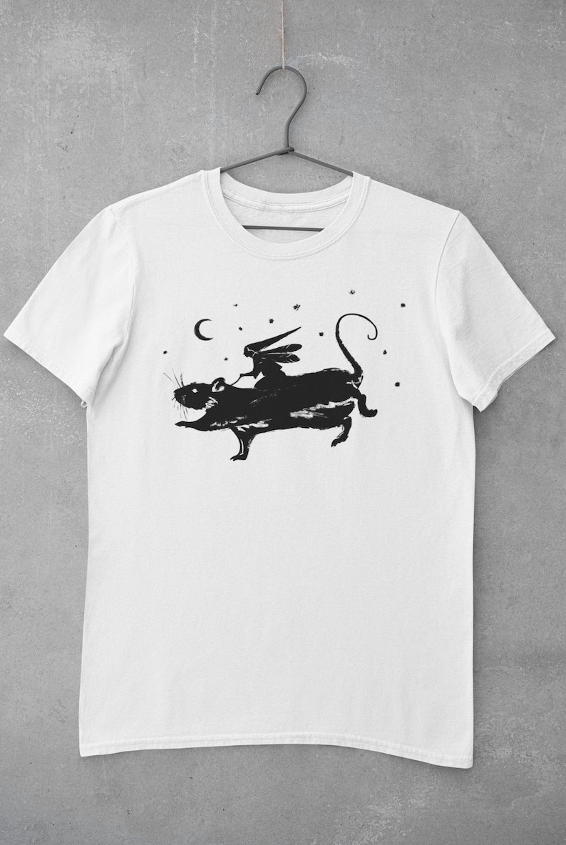 Puede incluir: Camiseta blanca con una silueta negra de un hada montando una rata bajo una luna creciente y estrellas.