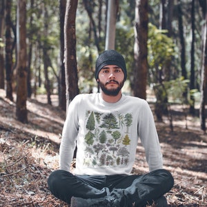 Puede incluir: Una sudadera blanca de manga larga con una ilustraci&oacute;n bot&aacute;nica vintage de varios &aacute;rboles. La sudadera la lleva puesta una persona sentada en un entorno boscoso.