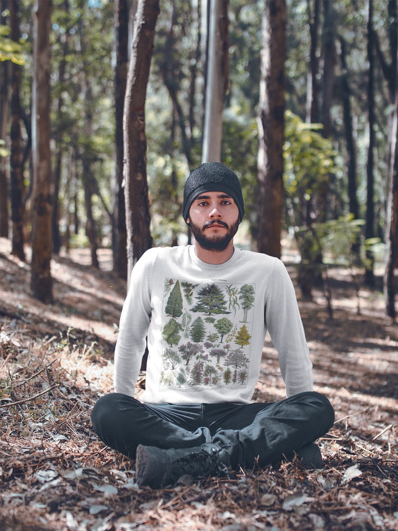 Puede incluir: Una sudadera blanca de manga larga con una ilustraci&oacute;n bot&aacute;nica vintage de varios &aacute;rboles. La sudadera la lleva puesta una persona sentada en un entorno boscoso.