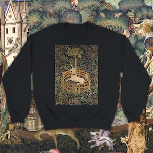 Op de afbeelding: Zwart sweatshirt met een print van de Unicorn Tapestries, een beroemd middeleeuws kunstwerk dat een eenhoorn laat zien die gevangen zit in een ronde omheining.