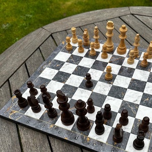 May include: A black and white chessboard with black and white chess pieces. The chessboard has a marble-like design with gold accents. The chess pieces are arranged in a game in progress.