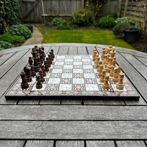 May include: A wooden chessboard with black and white squares, featuring a decorative inlay design. The board is set up with black and white chess pieces, with the white pieces on the right side and the black pieces on the left side.