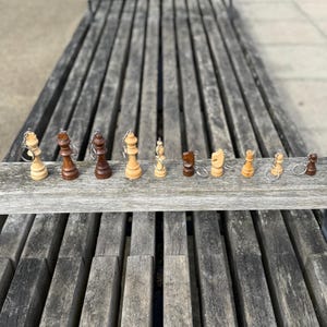 May include: A collection of miniature chess piece keychains in various colors, including light and dark wood tones. The pieces are arranged on a wooden plank, showcasing the king, queen, bishop, knight, rook, and pawn. The keychains are attached with silver metal rings.