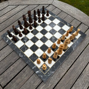 May include: A black and white marble chessboard with black and white chess pieces. The board is set up for a game of chess with the white pieces on the bottom and the black pieces on the top. The board is on a wooden table.