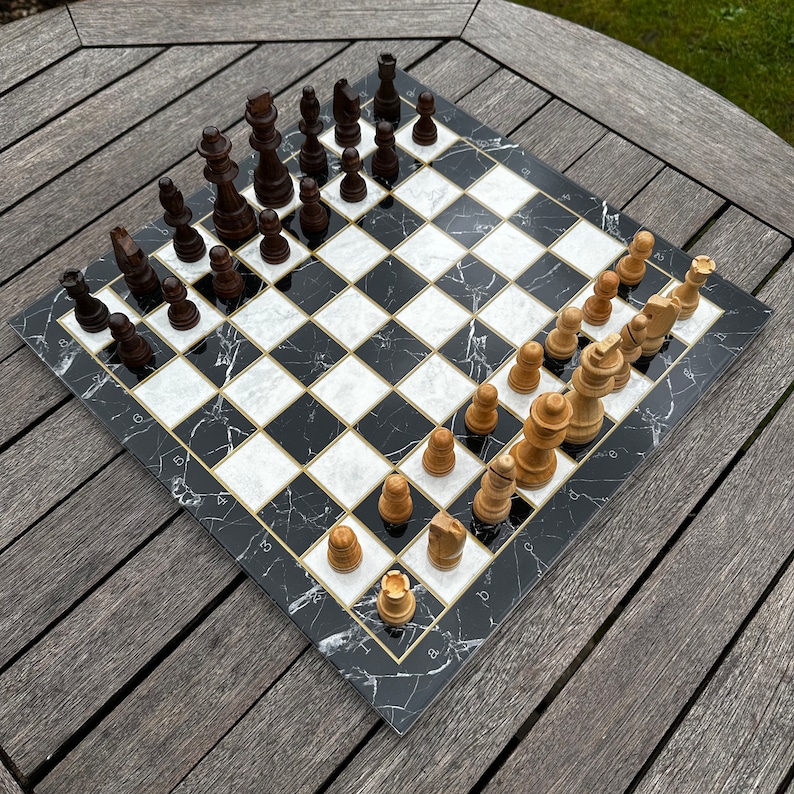 May include: A black and white marble chessboard with black and white chess pieces. The board is set up for a game of chess with the white pieces on the bottom and the black pieces on the top. The board is on a wooden table.