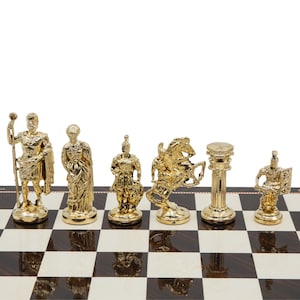 Op de afbeelding: Een set gouden schaakstukken op een zwart-wit geblokt bord. De stukken omvatten een koning, koningin, paard, loper, toren en pion. De stukken zijn gemaakt van metaal en hebben een gedetailleerd ontwerp.