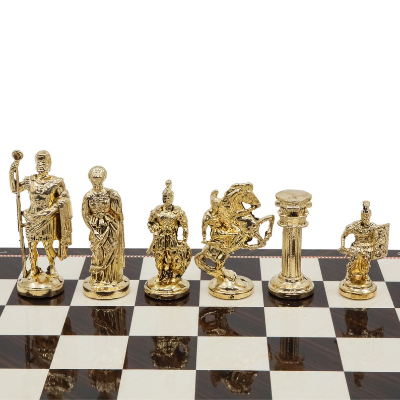 Op de afbeelding: Een set gouden schaakstukken op een zwart-wit geblokt bord. De stukken omvatten een koning, koningin, paard, loper, toren en pion. De stukken zijn gemaakt van metaal en hebben een gedetailleerd ontwerp.