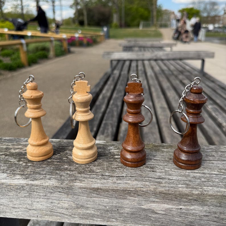 May include: Four wooden chess piece keychains. Two are light-colored, and two are dark brown. Each keychain features a chess piece design, including a queen and a king, and a silver-colored chain and ring.