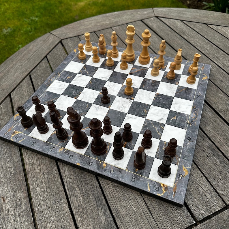 May include: A black and white chessboard with black and white chess pieces. The chessboard has a marble-like design with gold accents. The chess pieces are arranged in a game in progress.