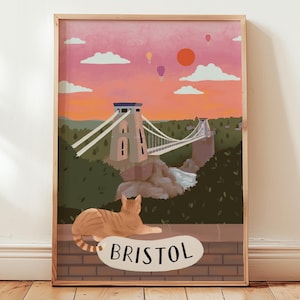 Könnte beinhalten: Gerahmter Kunstdruck mit der Clifton Suspension Bridge in Bristol, England, bei Sonnenuntergang. Eine getigerte Katze liegt auf einer Backsteinmauer mit dem Wort "Bristol" darunter. Das Kunstwerk hat eine warme Farbpalette.