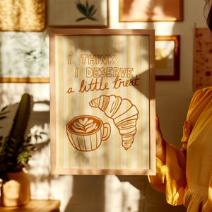 Framed coffee and croissant poster hanging in a gallery, adding a Parisian breakfast aesthetic.