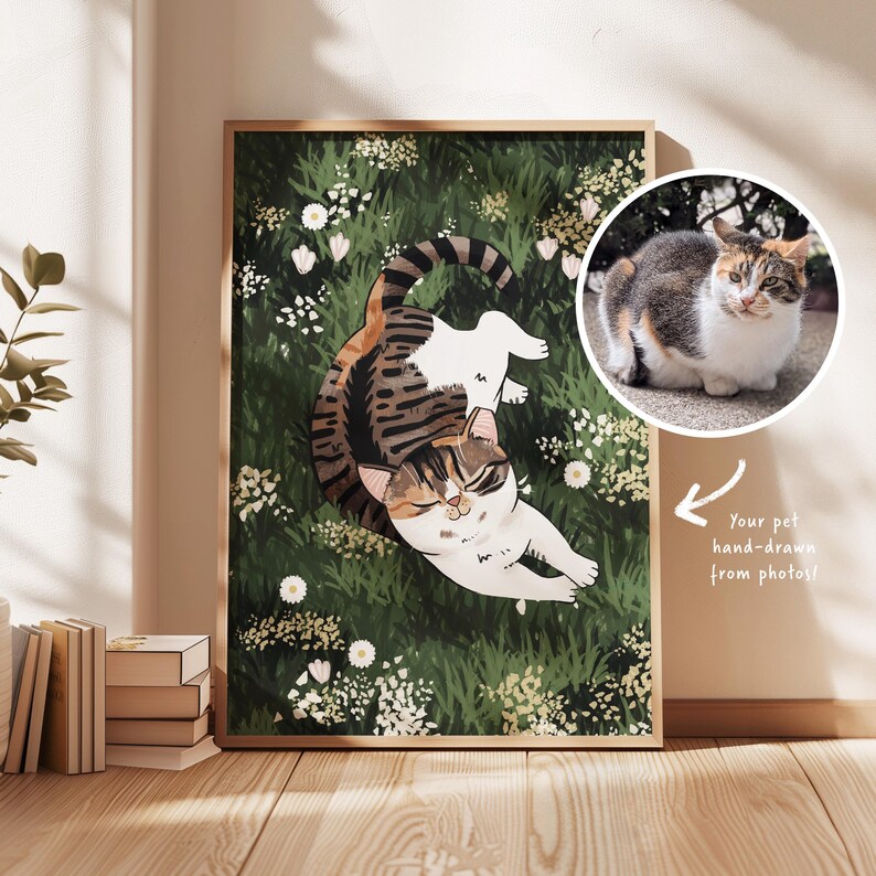 May include: A hand-drawn illustration of a cat in a field of flowers. The cat is brown, white, and black with green eyes. The flowers are white and pink. The illustration is framed in a wooden frame.