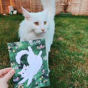 An example of a white fluffy cat next to the print.
