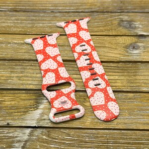 May include: Two red and white watch straps with a heart pattern. The straps are made of a flexible material and feature a repeating design of white hearts and small red dots. The straps are designed to fit a smartwatch.
