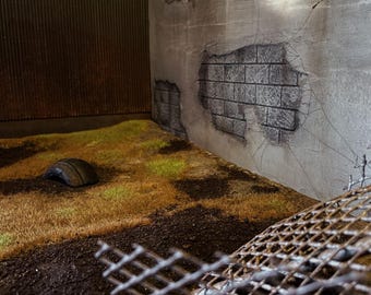 May include: A close-up of a rusty metal grate lying on the ground. The grate is broken and bent, and there is dirt and grass around it. There is a tire in the background.