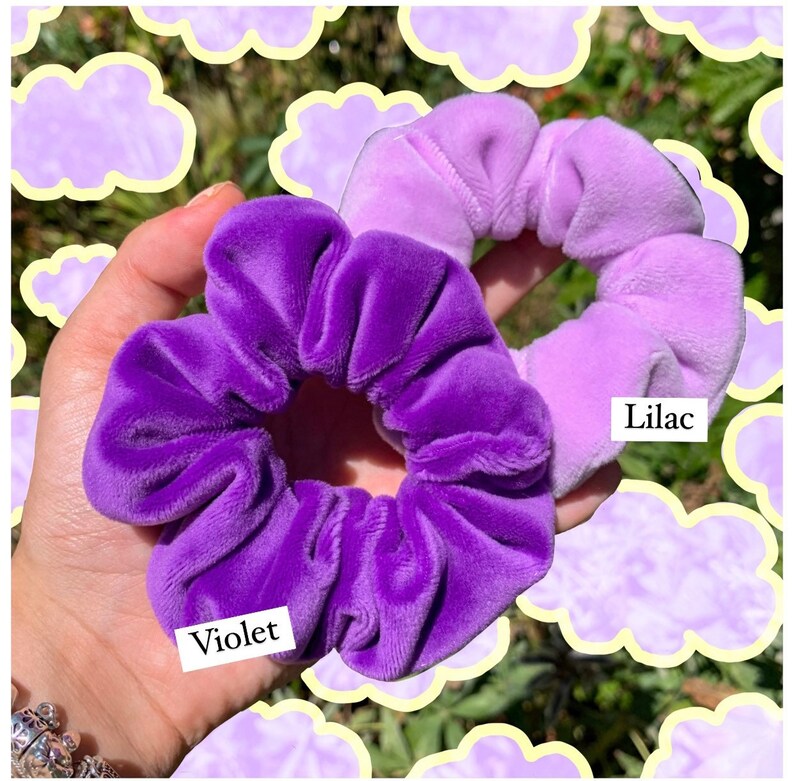 May include: Two velvet scrunchies in shades of purple. The scrunchie on the left is a solid dark purple labeled "Violet". The scrunchie on the right is a light purple ombre scrunchie labeled "Lilac".