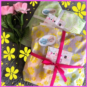 May include: Three gifts wrapped in yellow, green, and white patterned tissue paper with pink polka dot ribbon. The gifts are tied with a pink ribbon and have a handwritten tag that says "Scrunchhems Scrunchies by Emily".