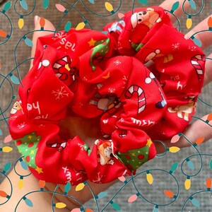 Puede incluir: Gomas para el pelo rojas con temática navideña y diseños festivos. La tela presenta imágenes de Papá Noel, bastones de caramelo, árboles de Navidad y copos de nieve. Las gomas están fruncidas y parecen suaves, perfectas para añadir un toque festivo a cualquier peinado.