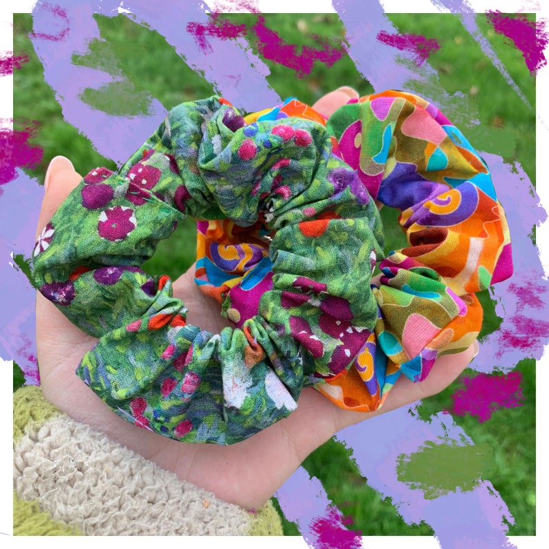 K&ouml;nnte beinhalten: Zwei bunte Haargummis mit floralen und abstrakten Mustern. Eines hat einen gr&uuml;nen Hintergrund mit rosa und lila Blumen. Das andere hat eine Mischung aus orange, lila und gr&uuml;nen Formen. Diese Haaraccessoires sind ideal.