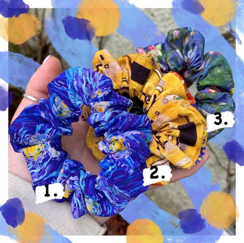 K&ouml;nnte beinhalten: Drei Stoff-Haargummis mit k&uuml;nstlerischen Mustern. Eines ist blau mit einem Sternennacht-Design, ein anderes ist gelb mit einem Geb&auml;udedesign und das dritte ist gr&uuml;n mit einem floralen Design. Die Haargummis werden in einer Hand gehalten.