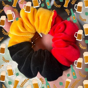 Puede incluir: Una goma para el pelo scrunchie de color negro, amarillo y rojo. El scrunchie está hecho de tela suave y peluda.
