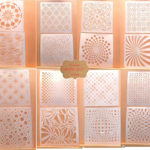 May include: Twelve different laser cut stencils on a wooden surface. The stencils are made of white mylar and feature geometric patterns.