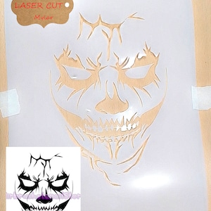 May include: A translucent Mylar stencil featuring a laser-cut design of a stylized, jagged skull face with sharp, angular features. A brown tag in the top left corner reads Durable LASER CUT Mylar. A small black and white reference image is included.