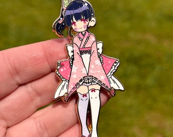 May include: A pink and white enamel pin featuring a cartoon character wearing a pink and white kimono with a butterfly design. The character has black hair and a pink bow. The pin has a gold finish.