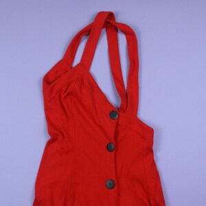 May include: A red sleeveless dress with a button-up front and a criss-cross strap detail at the neckline.