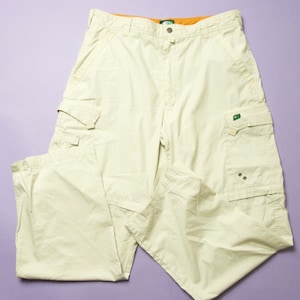 Könnte beinhalten: Eine beige Cargohose mit mehreren Taschen und einem grünen Logo am rechten Bein.