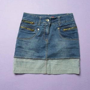 May include: A blue denim skirt with a light blue denim trim. The skirt has two pockets on the front with gold zippers.