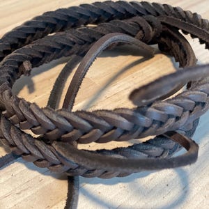 May include: A close-up of a brown leather cord, braided in a complex pattern. The cord is thick and durable, and it is perfect for crafting jewelry or other accessories.