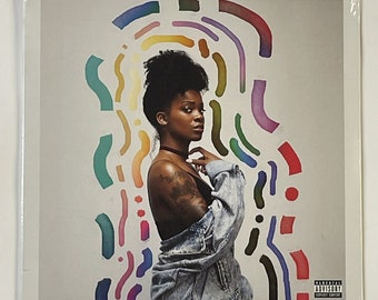 May include: A vinyl record cover featuring a woman with dark skin and short curly hair wearing a denim jacket. The background is a white surface with colorful abstract shapes.