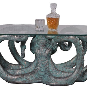 May include: A glass-top coffee table with an octopus base. The octopus is made of a green and brown resin and has a distressed finish. The table is perfect for a nautical themed living room.