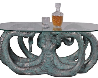 May include: A glass-top coffee table with an octopus base. The octopus is made of a green and brown resin and has a distressed finish. The table is perfect for a nautical themed living room.