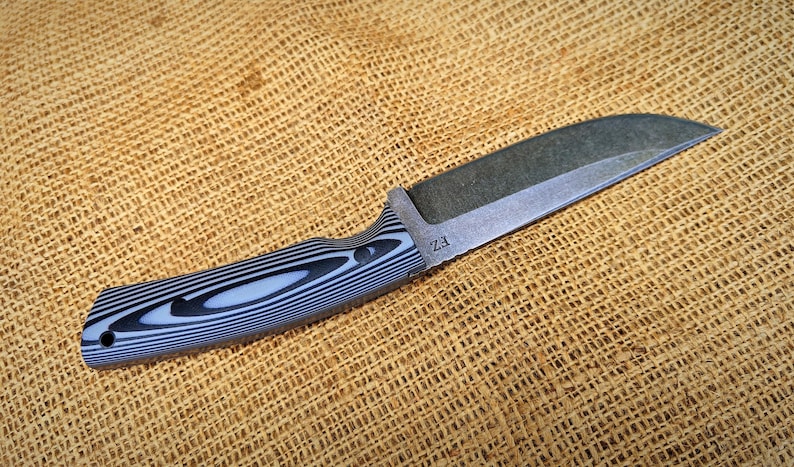 Op de afbeelding: Een mes met vast blad met een donker, getextureerd lemmet en een handvat met een zwart-wit gestreept patroon. Het mes heeft een full tang constructie en een gebogen lemmet. De handgreep is ergonomisch ontworpen voor een stevige grip. Het lemmet heeft de tekst "Z3".